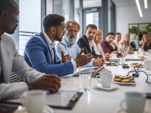 In a tabletop exercise, school professionals sit around a table and listen to the speaker, a Black man.